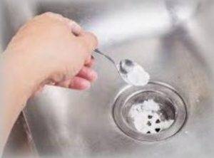 Pouring Vinegar and Baking Soda with spoon is a good method to unclog a double kitchen sink drain with standing water